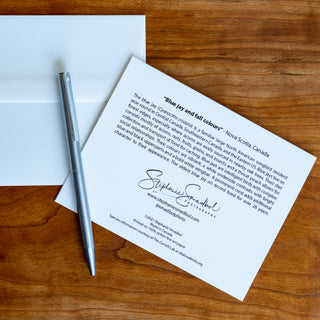 Back view of a blue jay wildlife notecard showing species description and lying flat on a table with a pen and envelope