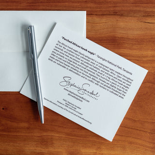 Back view of a perched hawk-eagle notecard showing species description and lying flat on a table with a pen and envelope