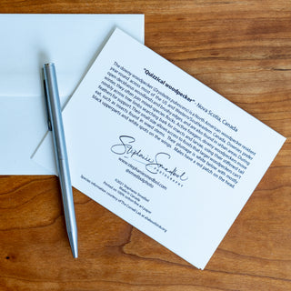 Back view of a woodpecker wildlife notecard showing species description and lying flat on a table with a pen and envelope