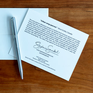 Back view of a song sparrow wildlife notecard showing species description and lying flat on a table with a pen and envelope